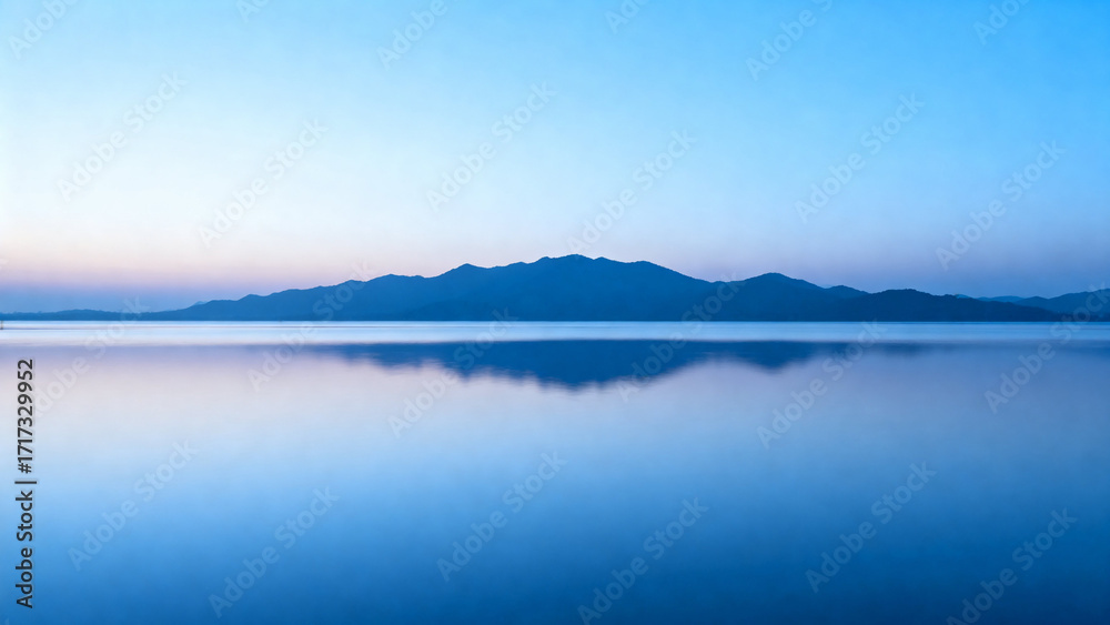 Fototapeta premium Calm lake reflecting distant mountains under a clear twilight sky