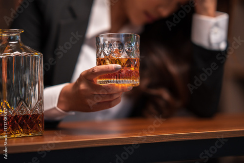 Asian woman in a black suit sitting holding a glass of whiskey at night in a restaurant.	