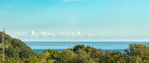 Relaxing landscape: the mountainous shore of the Black Sea, covered with green deciduous forest, the sea and light cumulus clouds above the horizon against the blue sky on a sunny summer day