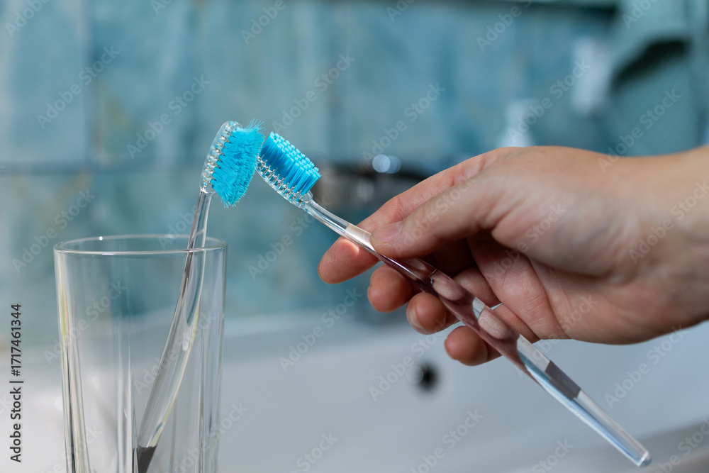 Fototapeta A person holds two toothbrushes above a glass, representing the importance of replacing brushes regularly