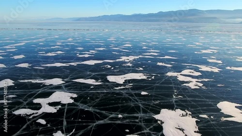 Flight forward above frozen Lake Baikal intricate ice cracks winter, Siberia. World's deepest freshwater lake with majestic mountains backdrop in Buryatia. Premier natural landmark for Arctic tourism