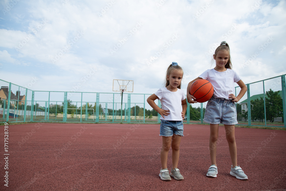 Obraz premium The children is having fun playing basketball in the yard on a warm summer day. Sports ground near the house for outdoor sports games