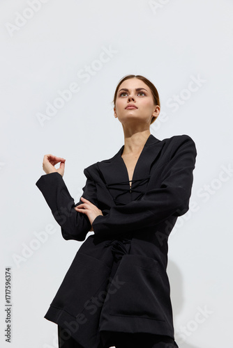 Tableau sur toile Fashion woman wearing black modern jacket poses against a plain light background with a confident and stylish expression, showcasing contemporary beauty and grace