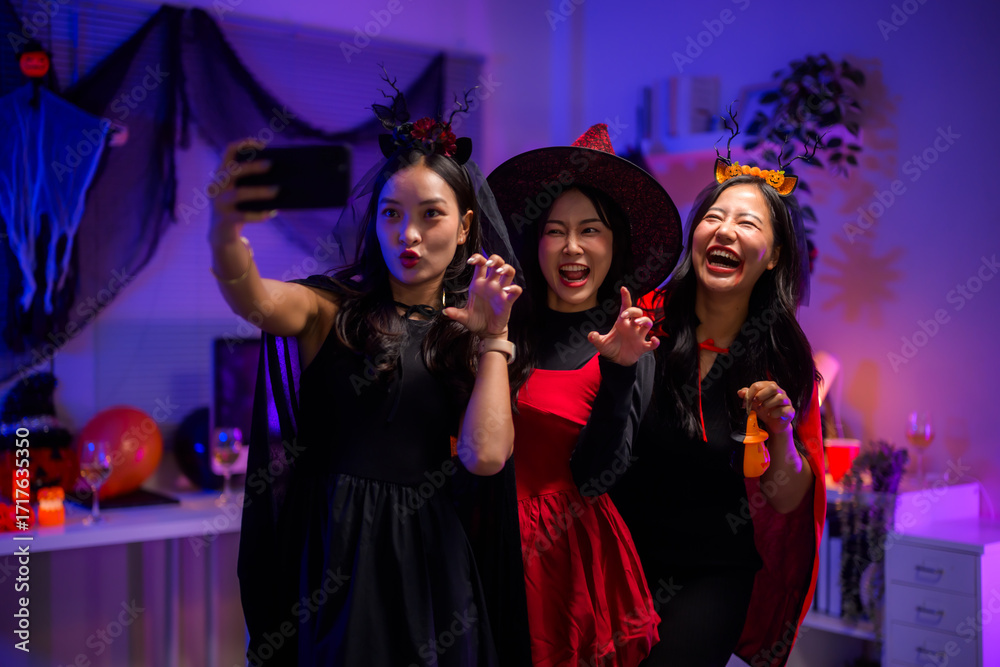 Obraz premium Young women friends celebrating Halloween, dressing up in costumes and taking selfie at party
