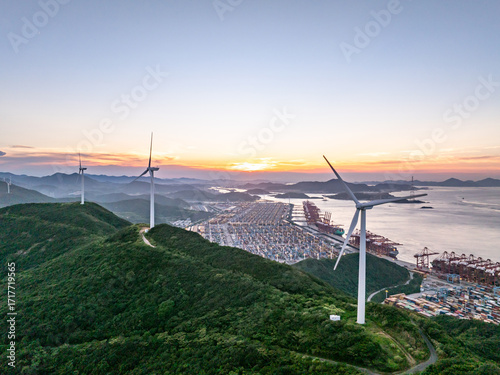 Photography Aerial view of wind turbines on a hill with a port and sunset in the background