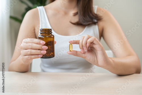 Dietary supplement concept, happy asian young woman hand holding fish oil pills, drugs medical tablet pouring capsules from medication bottle, take vitamin treatment for skin, hair at home, healthcare
