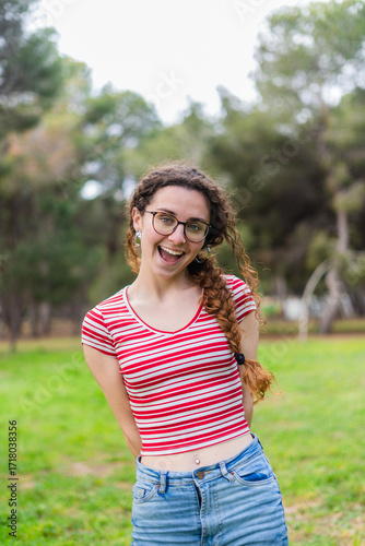 Portrait of a cheerful young woman with braided hair and glasses smiling in a park