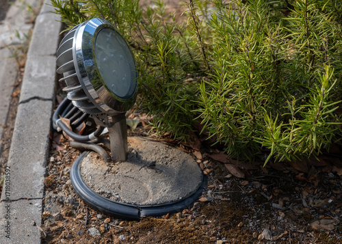 Outdoor Ground Spotlight With Metal Frame Illuminating Garden Bed And Rosemary Bush At Night In Landscape Design