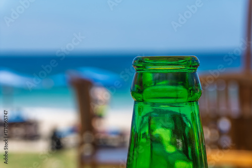 green glass beer bottle blur background of sunny beach blue ocean tropical getaway concept