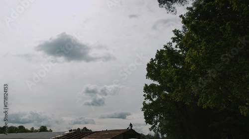 Two men repair the roof of long building on farm and put waterproofing material and slate on wooden beams.