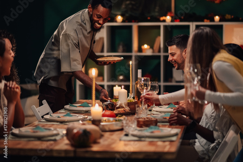 Fotografia Happy friends enjoying festive dinner, host serving food at candlelit table