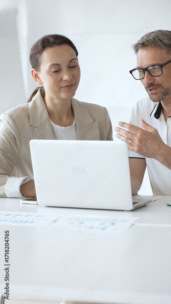 Obraz premium Businessman and adult businesswoman reviewing marketing analytics on laptops, working together strategically in contemporary workplace with minimalist interior design and collaborative atmosphere