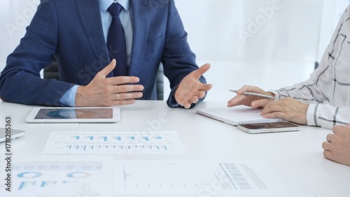 Business team engaging in a corporate meeting, discussing strategies while analyzing financial charts and graphs on a digital tablet alongside printed documents