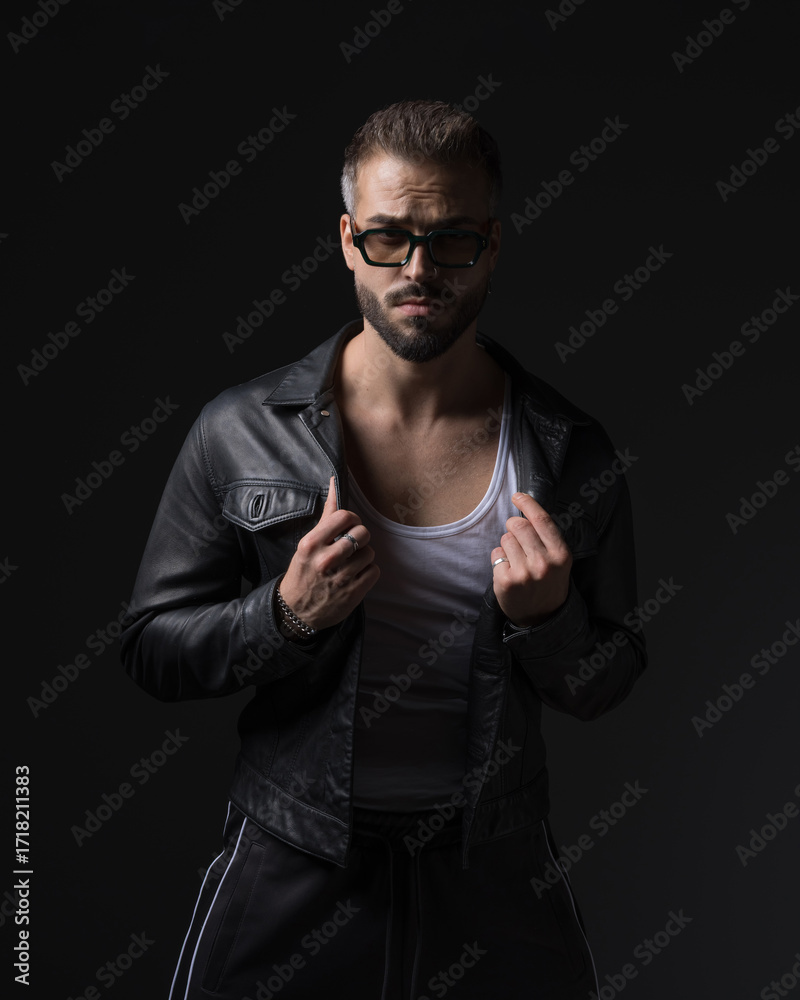 Naklejka premium cool fashion man with sunglasses pulling and adjusting black leather jacket