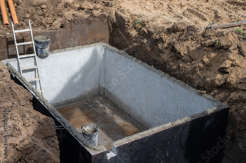 Concrete foundation pit with construction ladder and buckets at building site.
