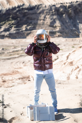 Person wearing astronaut helmet standing in desert landscape.