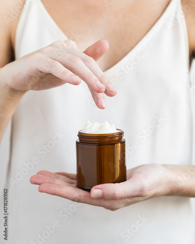 Woman's finger reaching for whipped beef tallow moisturizer in amber glass jar