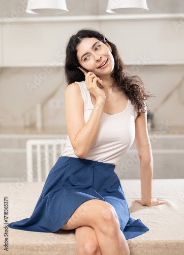 Portrait of smiling female who is talking by phone in the kitchen at home