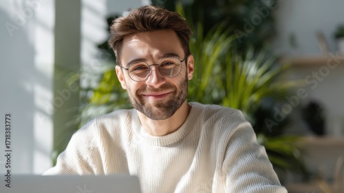 Smiling young man with glasses working on laptop in bright modern home interior.