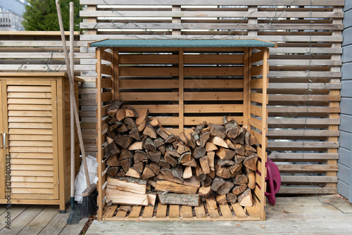 Wooden firewood storage near the house, next to it are garden tools.