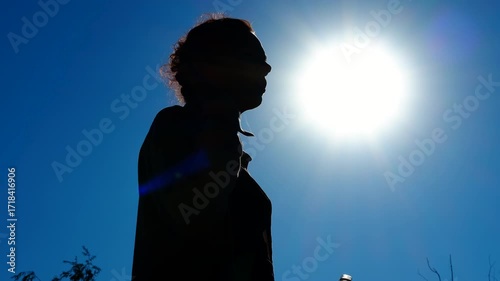 Woman drinking water under the sun silhouette montage. Silhouette of a woman drinking water from a plastic bottle under the scorching sun, relieving thirst and staying hydrated during a hot summer day