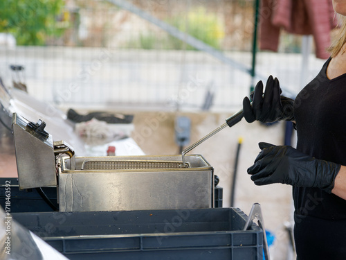 Préparation de frites dorées dans une friteuse professionnelle en acier inoxydable, scène de cuisine de rue ou de fête avec vendeuse au travail.
