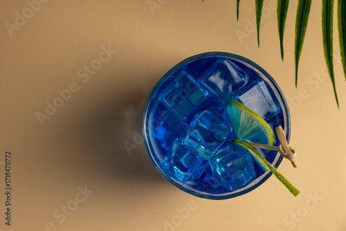 Colorful blue cocktail in a glass with a slice of lime on a beige background