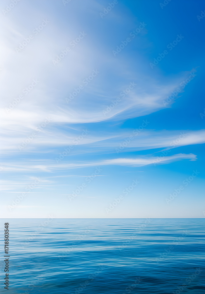 Fototapeta premium Tranquil seascape featuring calm, reflective water under a clear blue sky with soft, wispy clouds.