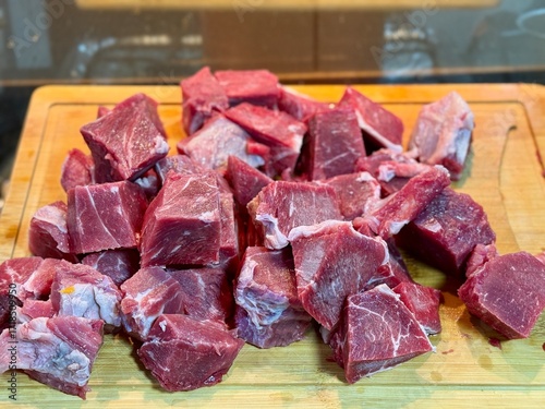 Carne em cubos cortas sobre a mesa com fundo desfocado e cebolas e panela con nivel de agua.