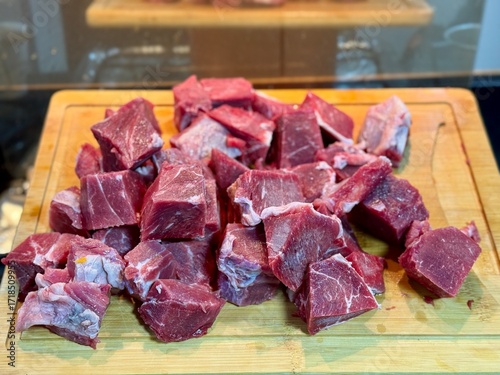 Carne em cubos cortas sobre a mesa com fundo desfocado e cebolas e panela con nivel de agua.