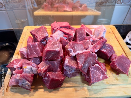 Carne em cubos cortas sobre a mesa com fundo desfocado e cebolas e panela con nivel de agua.