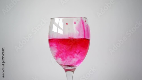 Red-painted coin drops into a clear glass of water, creating splash, ripples, and swirling dye — a concept of value contamination, cause-and-effect, and striking motion in liquid.