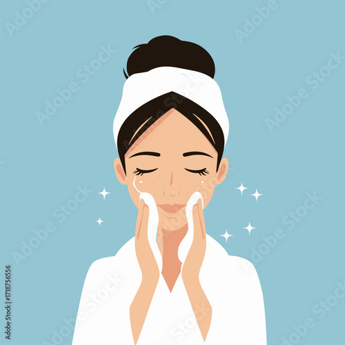 A woman is applying cleanser to her face while smiling, enjoying a rejuvenating skincare routine. She wears a headband and bathrobe, creating a tranquil atmosphere.