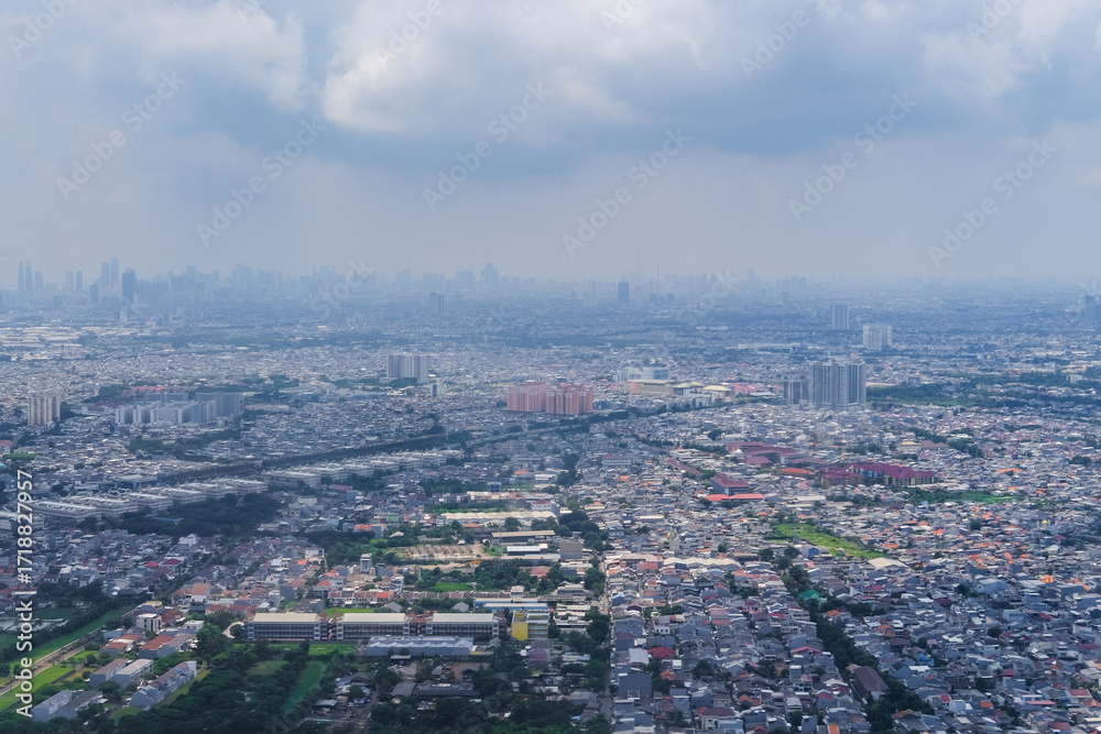 Obraz premium Aerial view of an urban cityscape seen from an airplane during landing, showing dense buildings, roads, and green areas under cloudy skies that create a calm metropolitan atmosphere.