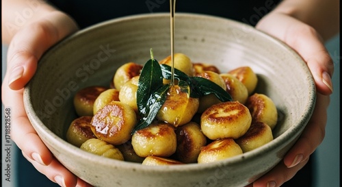 Golden pan-seared gnocchi in a rustic ceramic bowl with crispy sage leaves and a drizzle of glistening olive oil for gourmet dining
