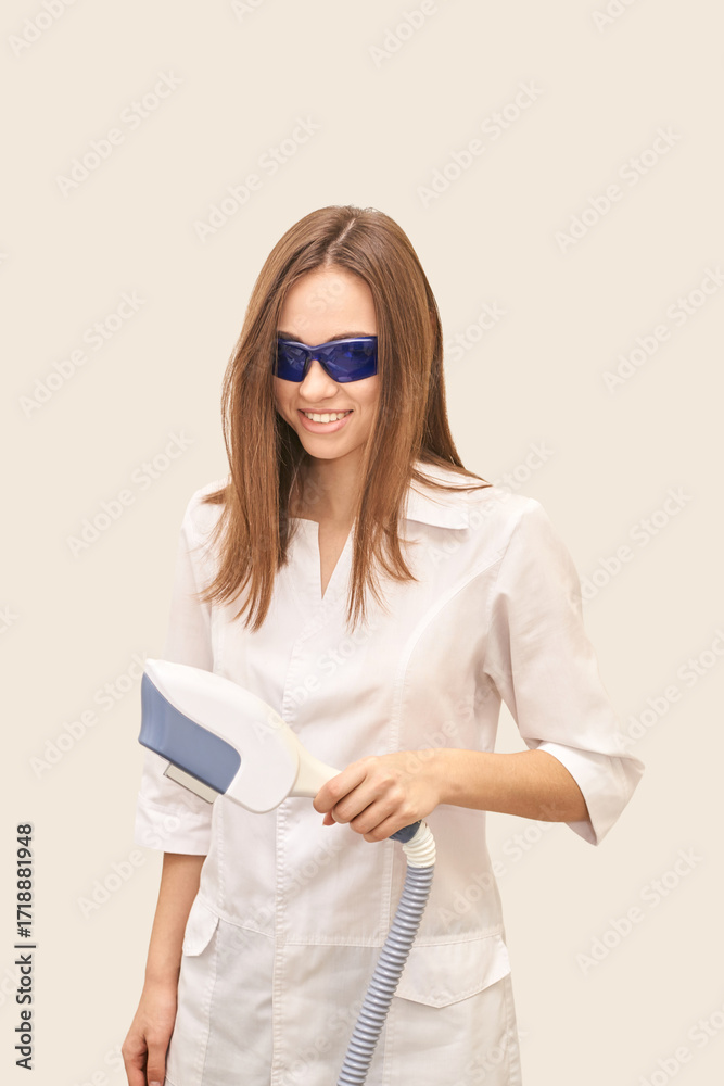 Fototapeta premium Young caucasian female in white coat holding laser device wearing protective glasses in a medical setting.