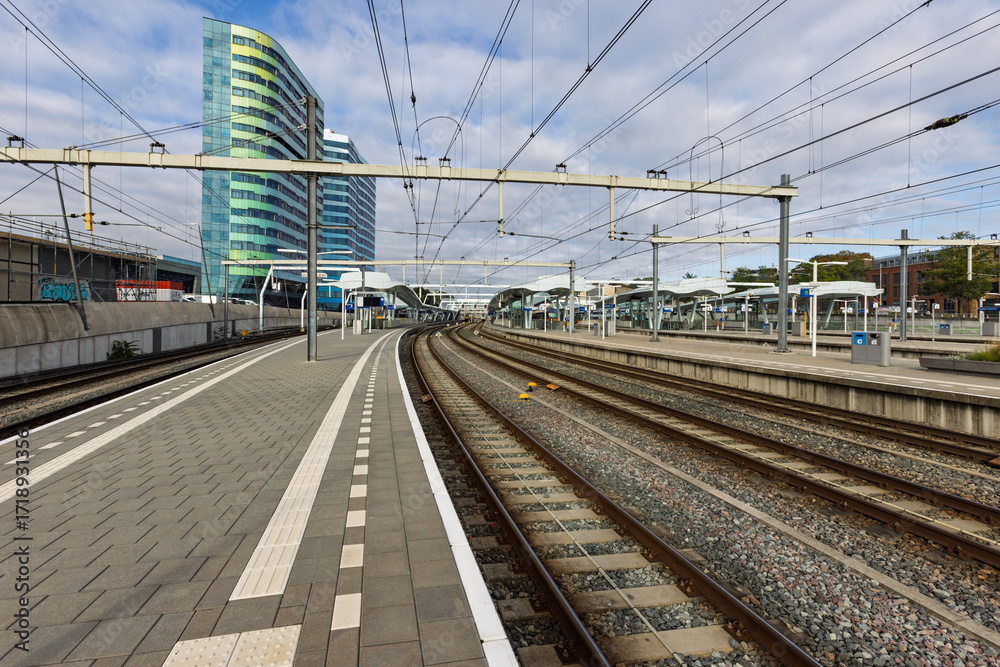 Fototapeta premium A view of the train tracks and platforms at Arnhem Central Station. The unique architecture of the station building and a modern office building are visible. Arnhem, Netherlands. 19 September 2025.
