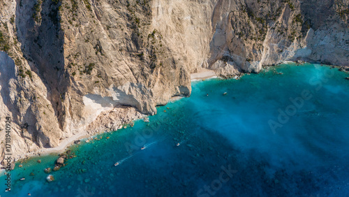 Aerial view of steep limestone cliffs with narrow sandy beach turquoise Ionian Sea clear shallow water and dramatic coastline in bright sunlight