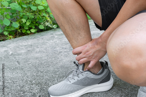 Принти на полотні Athlete checks ankle after outdoor run—possible sprain, tendon strain, or overuse injury from poor landing mechanics or fatigue