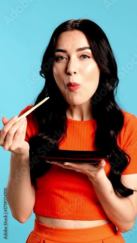 Woman with chopsticks eating sushi against a blue background