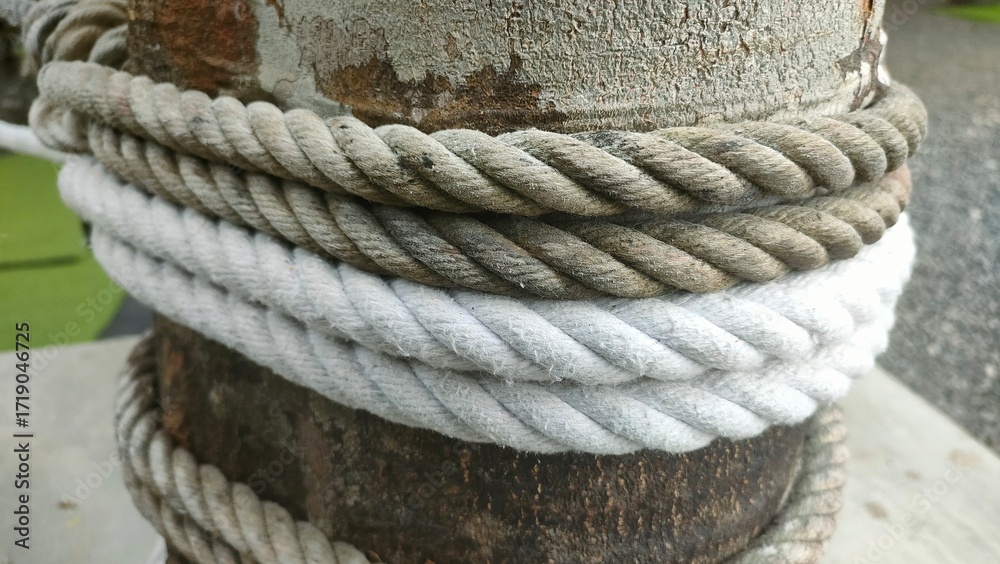 Fototapeta premium Close-up of coiled ropes wrapped around a weathered metal post with rust and peeling paint. Ideal for texture, nautical, industrial, or outdoor-themed visual content