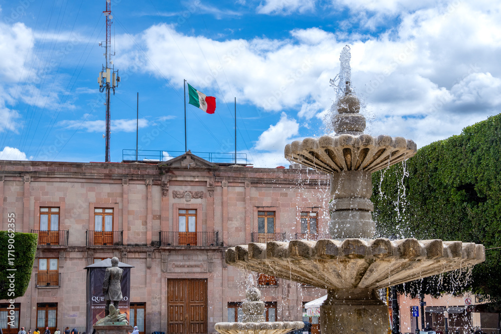 Fototapeta premium A fountain with a flag in the background. The flag is red, white and green. Historic center of Queretaro City, decorations and traditions to celebrate Mexico's Independence Day, colonial architecture,