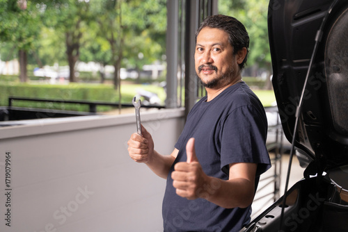 An Asian man and his tools are maintaining his car by himself.