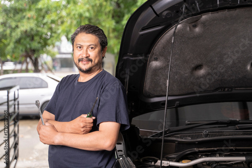 An Asian man and his tools are maintaining his car by himself.