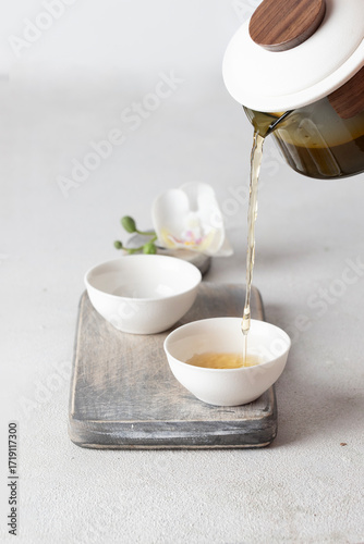 Pouringherbal tea into handcrafted cups, minimalist table setting with soft colors and natural textures, evoking peace, hospitality, and wellness culture.