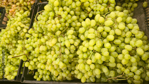 Green grapes in large boxes on store shelves. Fruit display and sale.