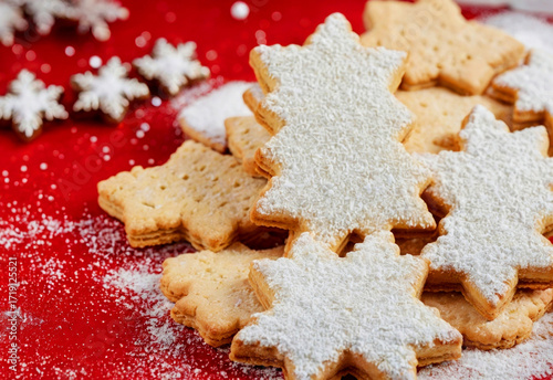 Decorative star-shaped cookies dusted with powdered sugar on a red background. Snowflake decorations scattered around.