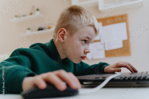 A boy with hearing aids focuses intently while playing a game on his laptop, showcasing modern adaptive technology and inclusive digital entertainment for children with hearing disabilities