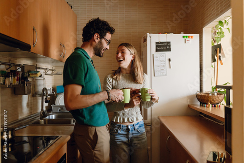 Fotografie A man and a woman laugh and hold cups while standing and looking at each other