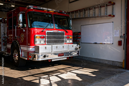 Red fire truck parked inside a fire station garage with sunlight casting shadows on the floor